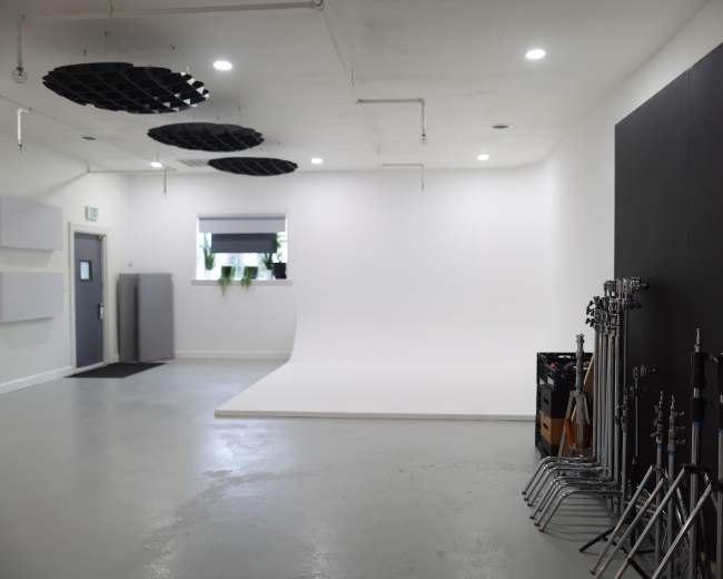 A spacious, well-lit studio with a white backdrop, a gray door, and various equipment stands arranged along one side.