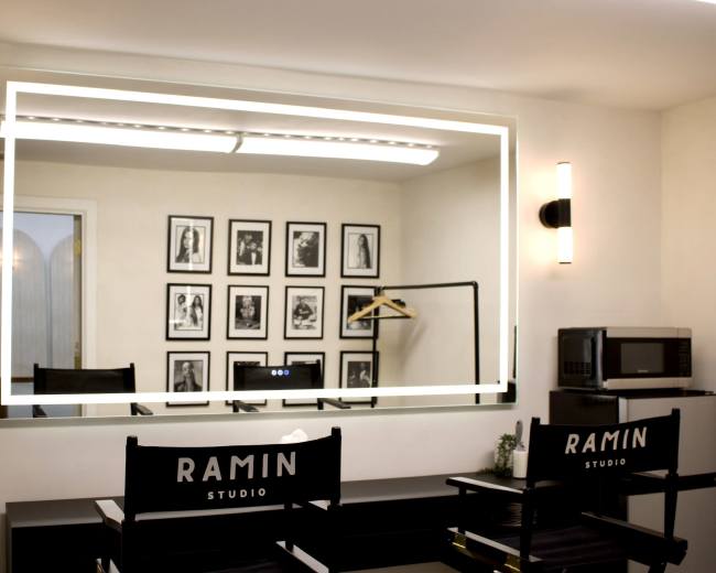 The image shows a modern studio space featuring a large illuminated mirror, black-and-white framed photos on the wall, and two director's chairs with the name "Ramin Studio."