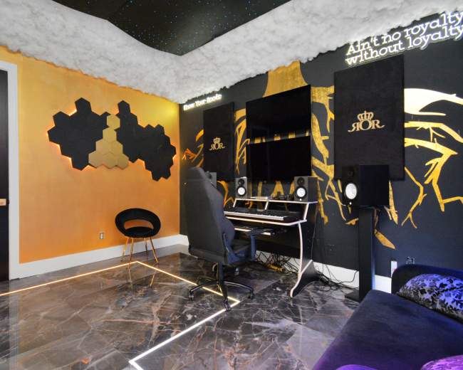 The image shows a modern music studio with a keyboard, speakers, and a wall decorated with geometric shapes and inspirational text under a cloud-like ceiling.
