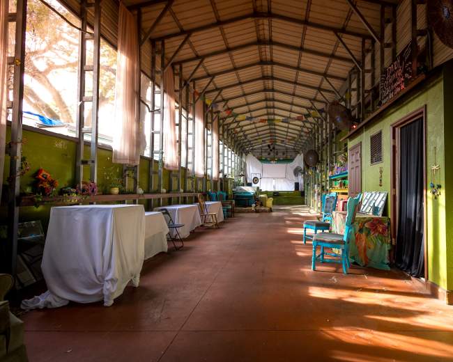 The image shows a long, narrow hall with high ceilings, featuring green walls, tables covered with white cloths, and colorful chairs along the sides.