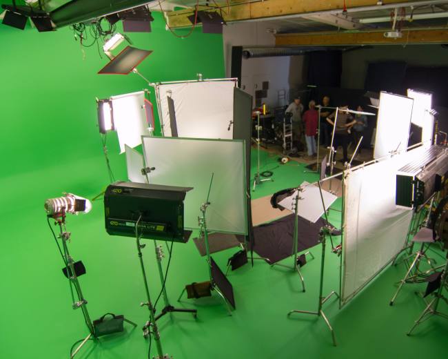 A film studio equipped with green screens and lighting tools is set up for a production.