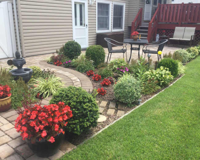 A well-designed garden features a winding stone path, neatly trimmed shrubs, colorful flower beds, and a seating area with a table and chairs.