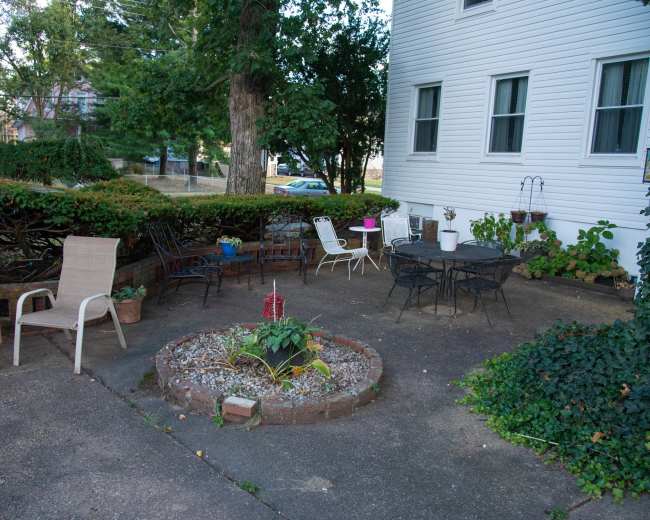 A patio area with various chairs, tables, and a circular garden bed surrounded by low plantings.