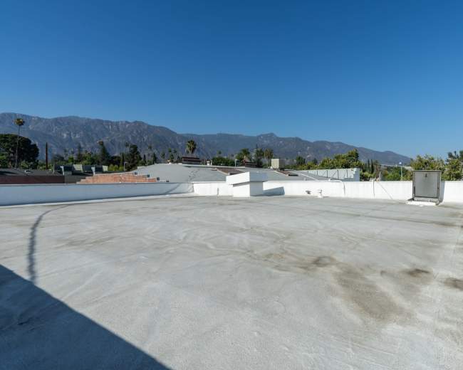 The image shows a flat, empty rooftop with a clear blue sky and distant mountains in the background.