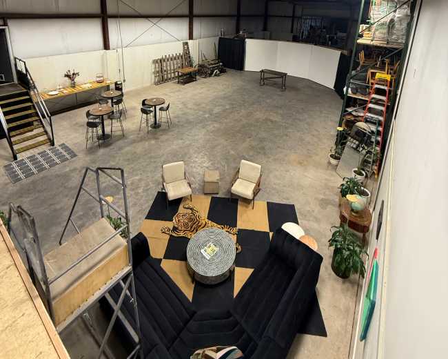 The image shows a large, empty warehouse space with seating arrangements and a circular performance area.