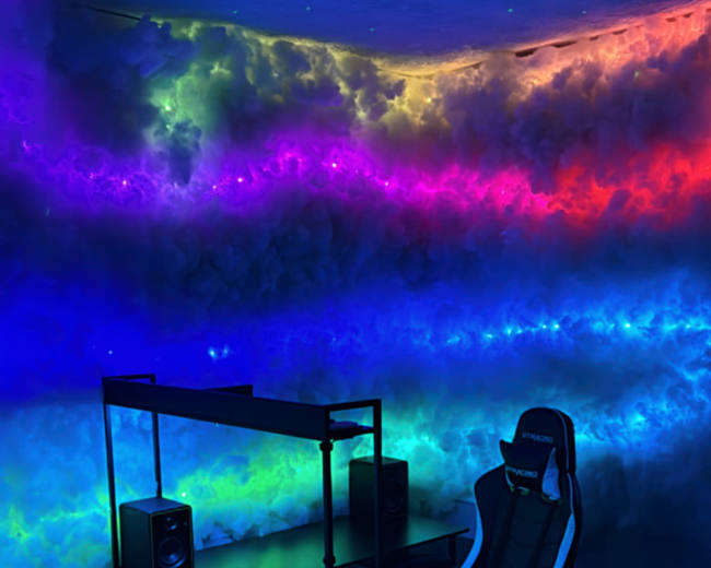 A modern workspace features a sleek desk and gaming chair, illuminated by colorful, cloud-like lighting on the wall.