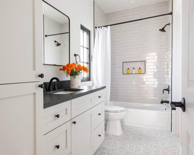A modern bathroom features a white vanity with a black countertop, a bathtub, and decorative wall tiles, complemented by a bouquet of orange flowers on the sink.