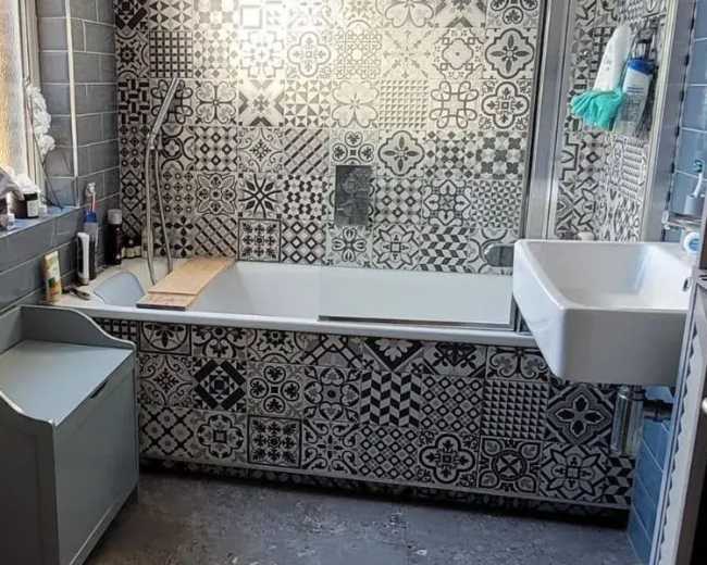 The bathroom features a bathtub surrounded by patterned tiles, a wall-mounted sink, and a heated towel rail.