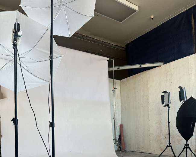 The image shows a photography studio with a white backdrop, lighting equipment, and cables on a concrete floor.