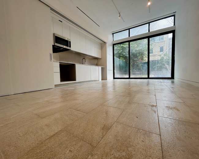 The image shows a modern, empty interior space with a kitchen area on one side and large sliding glass doors leading to an outdoor view.