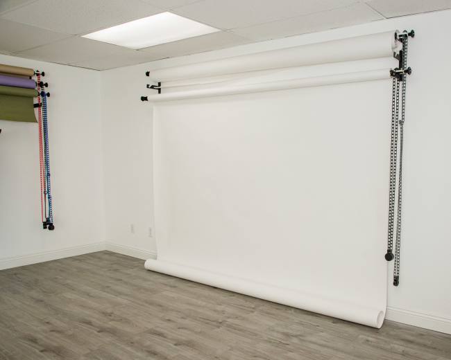 The image shows a clean, empty studio space with a white backdrop rolled down on a support system against a light-colored wall.
