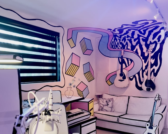 The image shows a colorful music studio with a white couch, a keyboard, and guitars displayed on the walls.