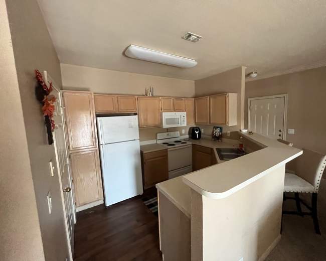 A kitchen features light wooden cabinets, white appliances, and a small breakfast bar with a chair.