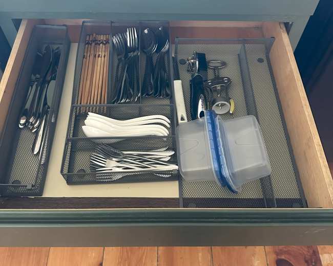 The image shows a kitchen drawer containing organized utensils, including knives, forks, spoons, chopsticks, and a plastic container.
