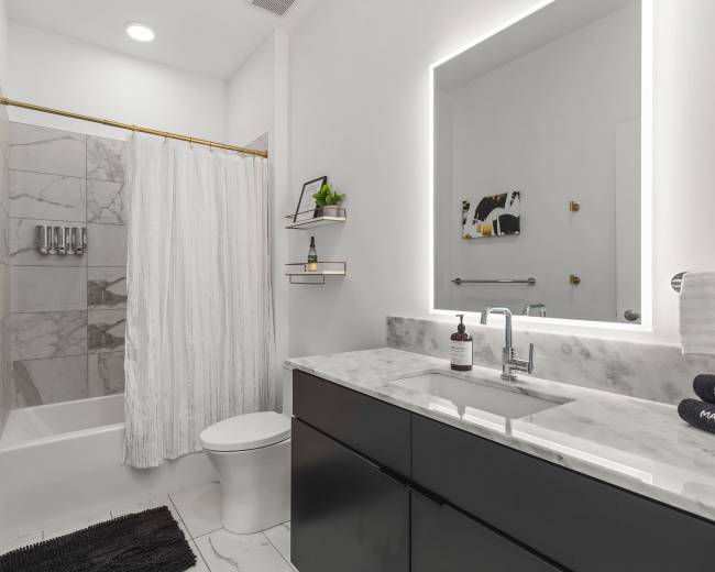 A modern bathroom features a bathtub with a shower curtain, a marble countertop sink, and shelves with toiletries.