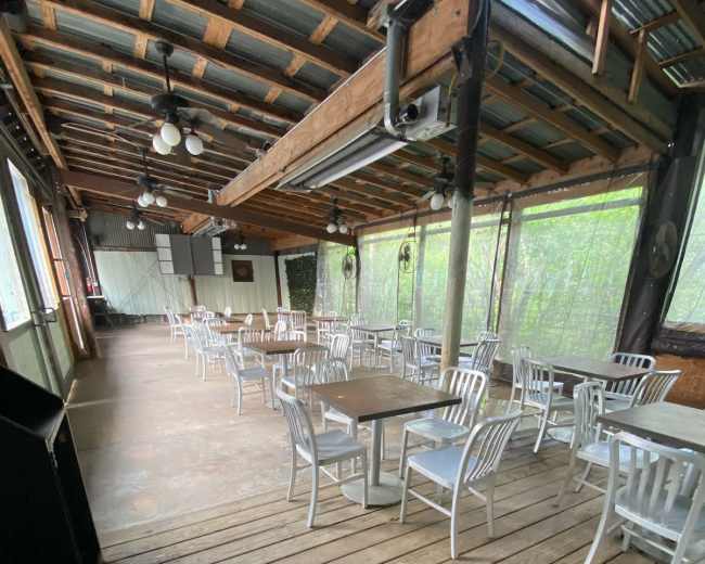 A spacious, empty dining area with wooden flooring and metal chairs arranged around small tables.
