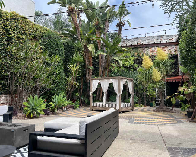The image features a landscaped garden with a seating area, a gazebo, and various tropical plants surrounded by brick walls.