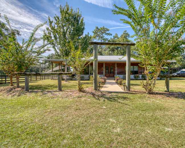 A wooden building surrounded by trees and a grassy area, with a pathway leading to the entrance.