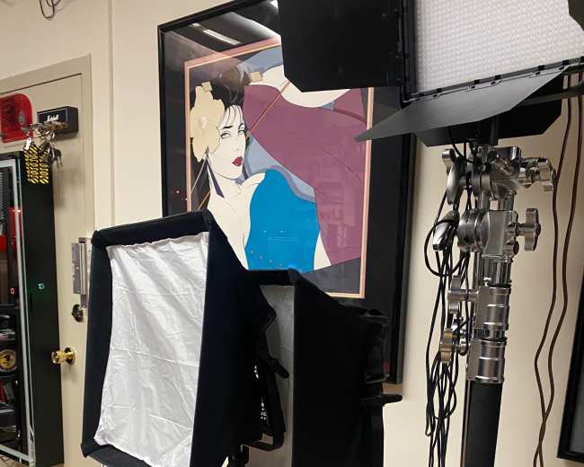 A photography studio setup with two softbox lights, a red stool, and a framed artwork on the wall.