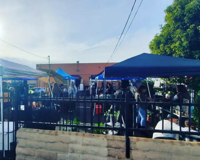 A bustling outdoor market scene is filled with vendors and customers under various tents and canopies.