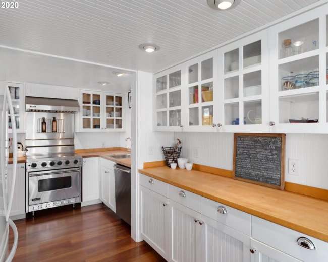 The image shows a modern kitchen with white cabinetry, stainless steel appliances, and wooden countertops.