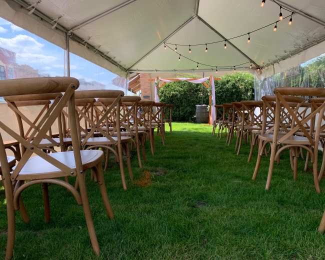 A tented area features rows of wooden chairs arranged on a grassy surface, with string lights overhead.