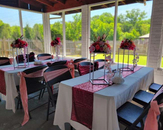 The image shows a decorated event space featuring tables set with floral centerpieces and pink table runners.