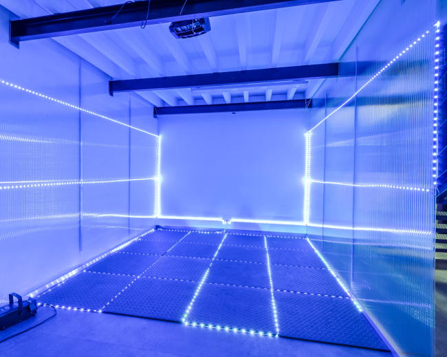 The image shows a room with a smooth floor and walls lined with blue LED lights, creating a minimalist and modern space.