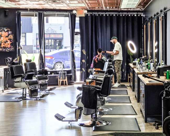 The image shows a hair salon with styling chairs, large mirrors, and a stylist working with a client, while sunlight streams through the windows.