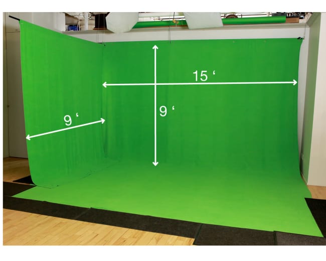 A green screen setup with dimensions indicated: 15 feet wide and 9 feet tall, placed on a floor with mats.