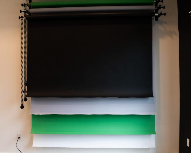 The image shows a wall-mounted backdrop installation featuring black, white, and green rolls of paper on a textured wall.