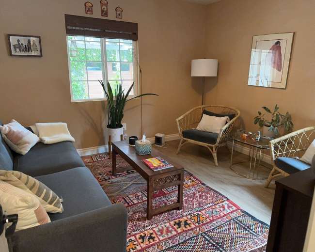 A cozy living room features a gray sofa, a wooden coffee table, a plant, and a light fixture, with artwork and a patterned rug complementing the space.