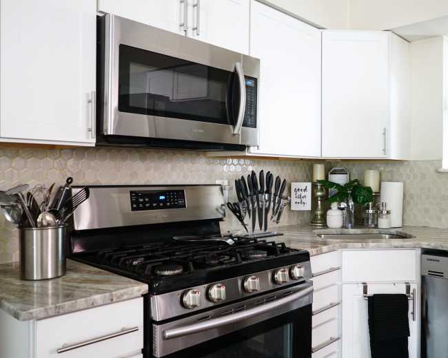 A modern kitchen features stainless steel appliances, including a microwave and a gas stove, with white cabinetry and a hexagonal backsplash.