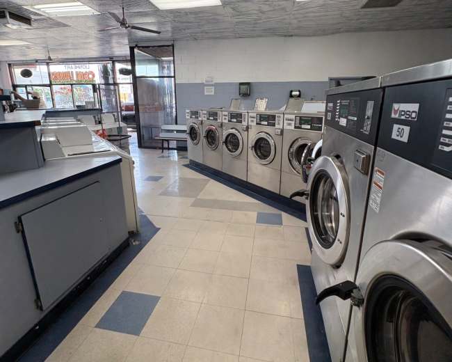The image shows a laundromat interior with rows of washing machines and a service counter visible in the foreground.