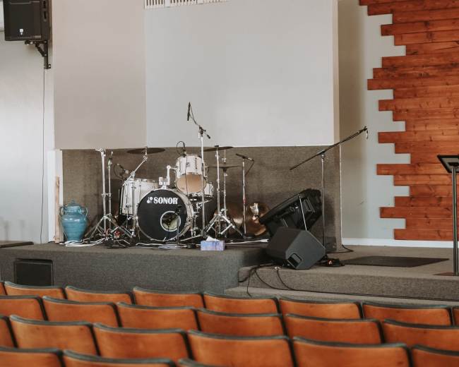 A stage with a drum set and microphones, accompanied by empty rows of brown seats in a music venue.