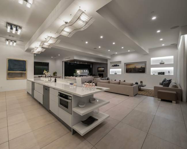 A modern, open-concept kitchen and living area with sleek, white cabinetry, a central island, and a spacious seating arrangement.