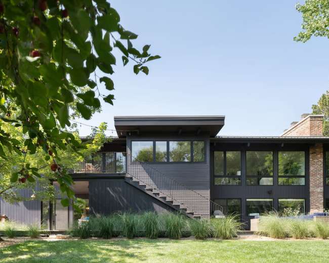 A modern two-story house features large windows and a sleek design, surrounded by greenery and grass.