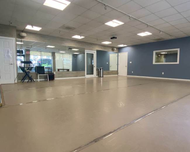 The image shows a spacious, empty room with a smooth floor, large mirrors on one wall, and a simple, functional design.