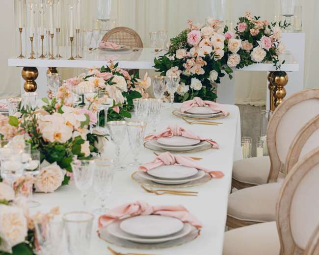 The image shows a elegantly set dining table adorned with floral arrangements and decorative tableware in a spacious, well-lit venue.