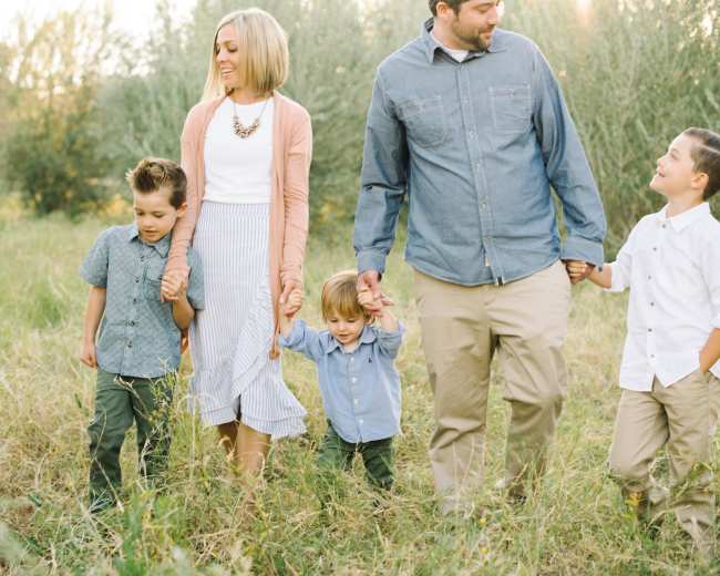 A family of five walks hand-in-hand through a grassy area with trees in the background.