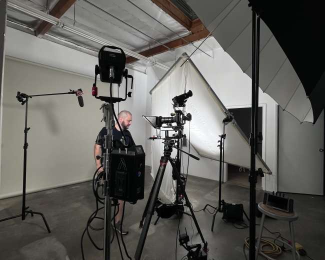A video production setup is arranged in a studio, featuring cameras, lights, and microphones.