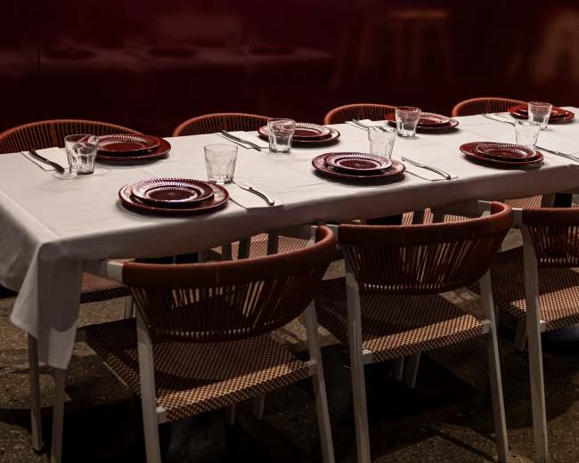 A dining table is set with red plates and glassware in front of a glowing restaurant sign that reads "Spiced Barangaroo Eclectic Indian."