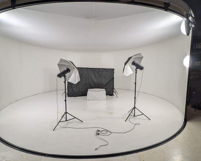 The image shows a photography studio setup with two light stands and a backdrop in a circular room with a white floor and walls.