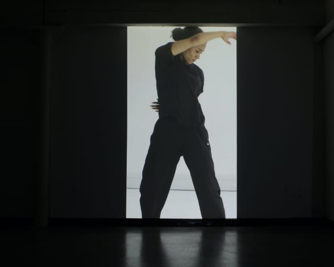 A dancer in a black outfit performs in front of a large, illuminated screen.