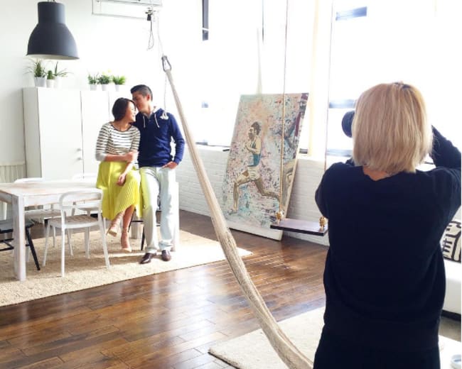 A photographer captures a couple posing in a brightly lit, modern room with wooden floors and contemporary decor.