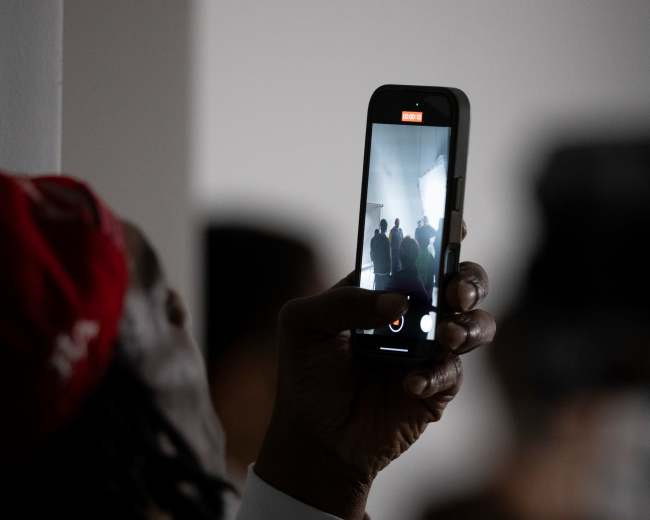 A person holds a smartphone to capture a photo of a group of people in a dimly lit space.