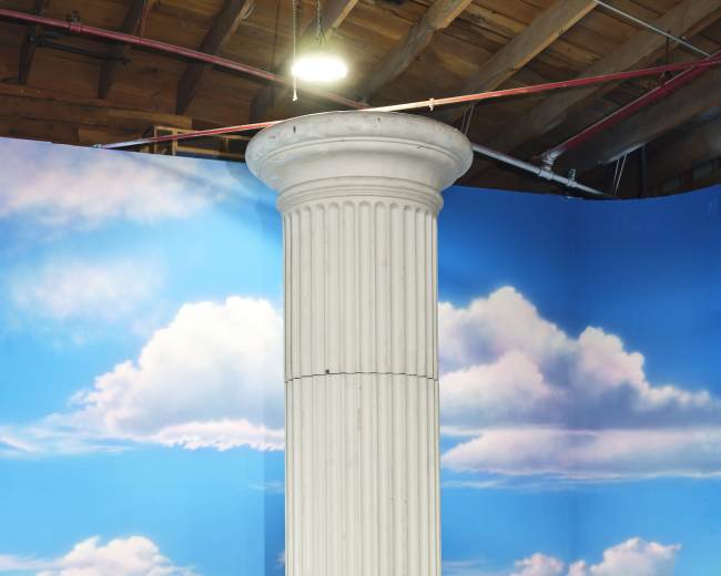 A white, fluted column set against a blue backdrop with painted clouds.