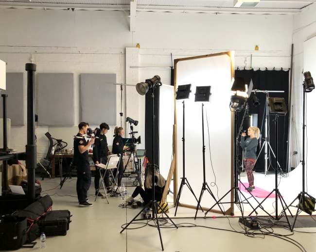 A studio setup shows a photographer and crew working with a model under bright lights against a backdrop.