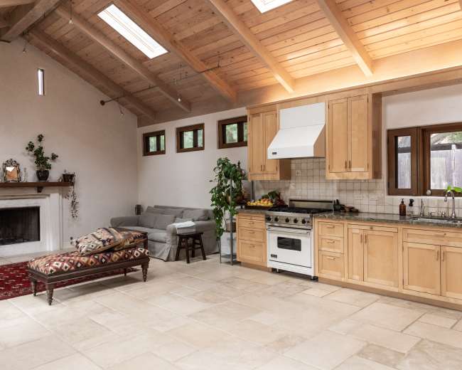 The image shows an open kitchen and living area with wooden beams, a fireplace, and a mix of furniture and decor.