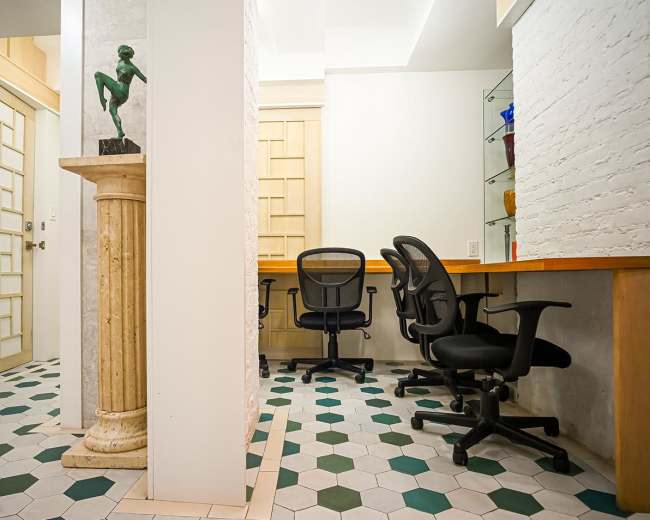 The image depicts a modern office space featuring three black office chairs, a decorative column with a statue, and a patterned hexagonal tile floor.